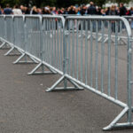 An aerial view of numerous metal barriers set up in a zigzag pattern on grass, indicating a waiting area for a large event.