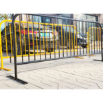 Black and yellow crowd barricade installed on a pavement, with cars parked in the background.