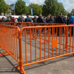 Bright orange crowd control barriers used to manage large crowds at an outdoor festival.