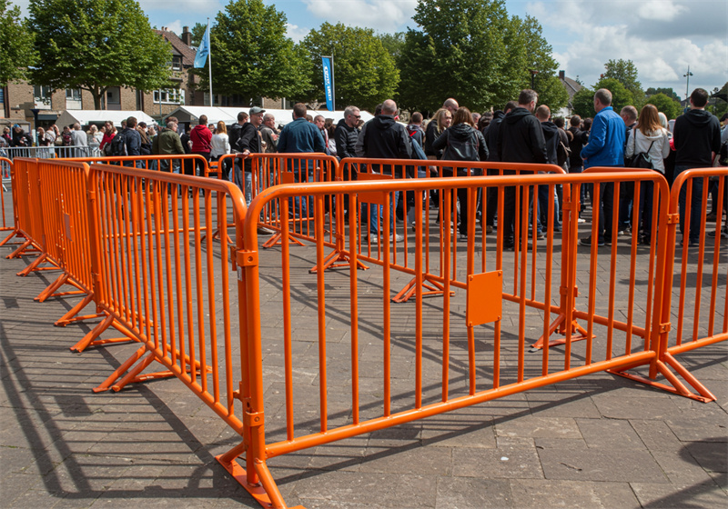 Bright orange crowd control barriers used to manage large crowds at an outdoor festival.