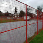 A red temporary fence set around an outdoor area, located along the edge of a sports field.