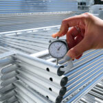 A close-up of a person using a caliper to measure the thickness of steel barricades, emphasizing quality control during manufacturing.