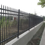 Installed black steel picket fence along a walkway, illustrating its application in a residential or commercial setting.