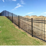 Metal black fencing on a hillside with blue sky background.