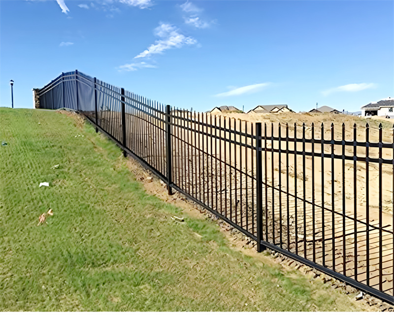 Metal black fencing on a hillside with blue sky background.