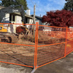 Temporary construction fence installed around a work site with machinery nearby, ensuring safety and demarcation of the area during excavation work.