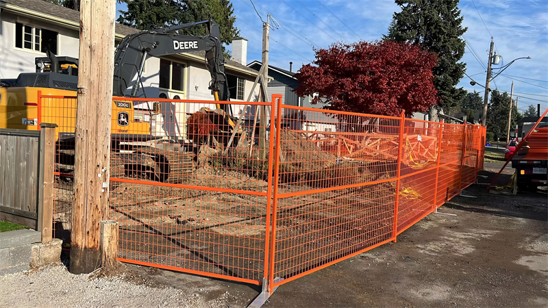 Temporary construction fence installed around a work site with machinery nearby, ensuring safety and demarcation of the area during excavation work.