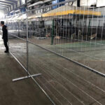 Silver temporary construction fence panels set up in an industrial environment with a worker overseeing the installation.