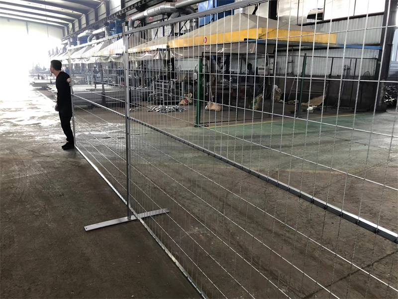 Silver temporary construction fence panels set up in an industrial environment with a worker overseeing the installation.