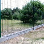 Green metal fence installed outdoors, with grass and trees nearby.