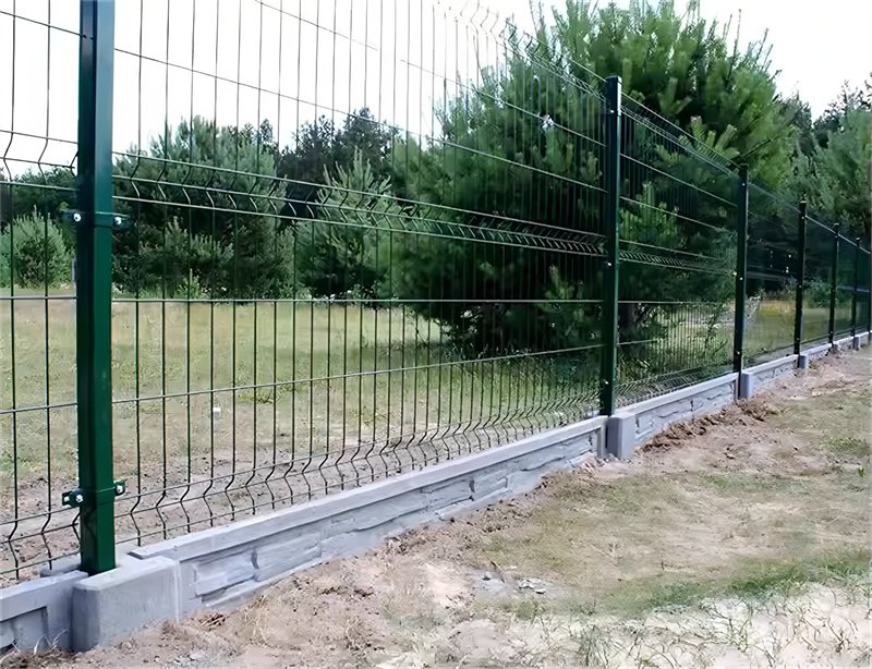 Green metal fence installed outdoors, with grass and trees nearby.