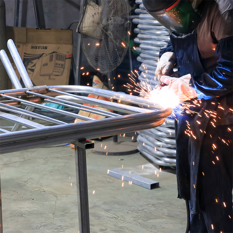 A worker welding a metal frame with sparks flying, surrounded by industrial tools and equipment.