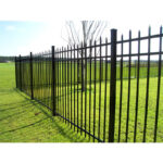 Installed steel picket fence surrounding a green field, emphasizing durability and aesthetic appeal in a natural setting.