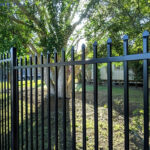 Black steel picket fence with pointed tops installed in a residential backyard with trees.