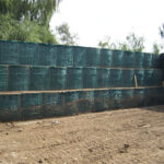An outdoor defensive wall constructed from multiple layers of Hesco barriers, filled with material and stacked for enhanced security.