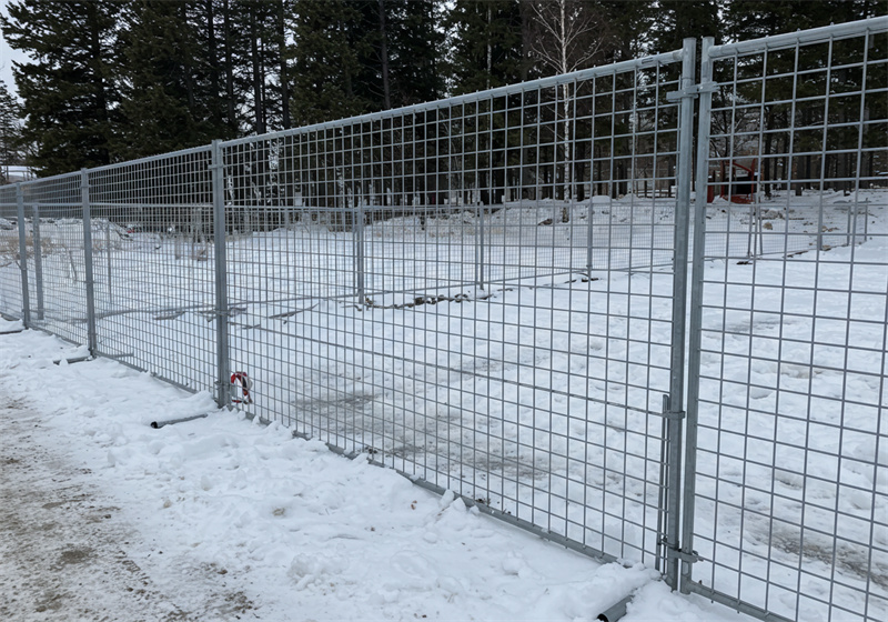 A series of gray metal temporary fences arranged in a snowy outdoor area, surrounded by trees.