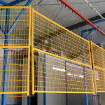 A yellow grid fencing panel hanging from a structure in a warehouse, showcasing the fencing's design and construction.
