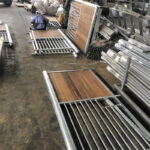 A workshop area with various components for horse stalls laid out, including wooden panels and metal frames being assembled by a worker.
