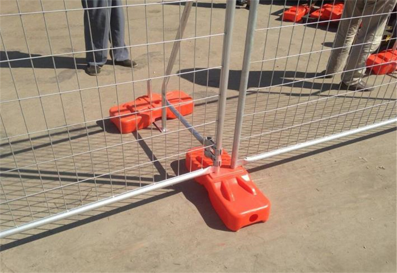 A detailed view of a temporary fence showing bright orange plastic bases used for stability, with the fence panels connected securely, indicating a well-assembled construction barrier.