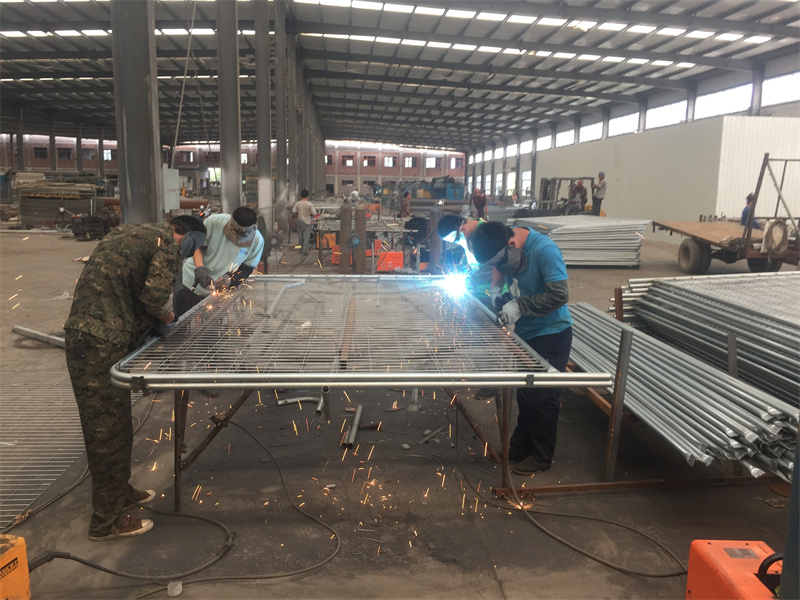 Workers welding and assembling metal fence panels in an industrial manufacturing facility.