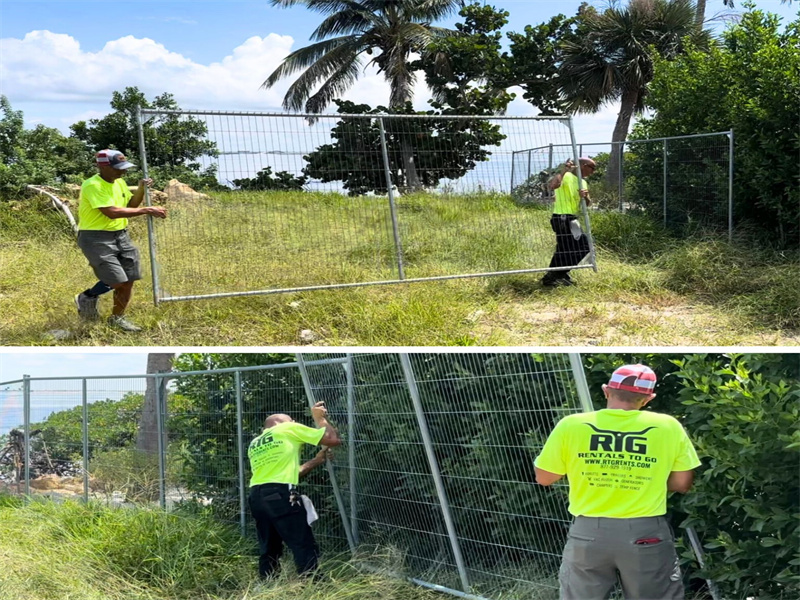 Workers installing temporary fencing panels in a grassy outdoor area surrounded by trees and vegetation.