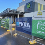 A construction site fenced off with banners displaying branding and safety messages, located outside a Woolworths store, with construction equipment visible in the background.