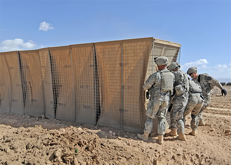 A group of soldiers installing a Hesco barrier in a desert environment for protective reinforcement and perimeter security.