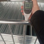 A close-up of a metal crowd control barrier with a thickness measurement gauge held against it. The display shows a reading of 80.1 micrometers, indicating the thickness of the barrier's coating.