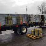 A truck loaded with metal fencing materials is parked, featuring several yellow-tipped bases stacked on the truck bed, ready for transport to a construction site.
