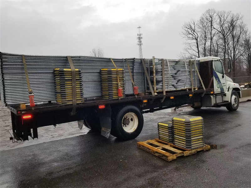 A truck loaded with metal fencing materials is parked, featuring several yellow-tipped bases stacked on the truck bed, ready for transport to a construction site.