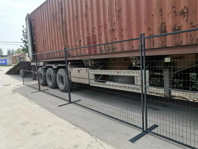 A close-up view of a wire mesh fence alongside a large shipping container truck, highlighting the fence's structure and the vehicle's wheels. The truck is parked on a concrete surface.