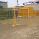 A section of bright yellow temporary fencing is displayed, showing its grid design. The fence is secured with concrete bases on a dirt surface, indicating its use for crowd control or construction sites.