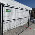 A black metal fence adjacent to a white tent, featuring a "Sunbelt Rentals" sign, set under a clear blue sky.