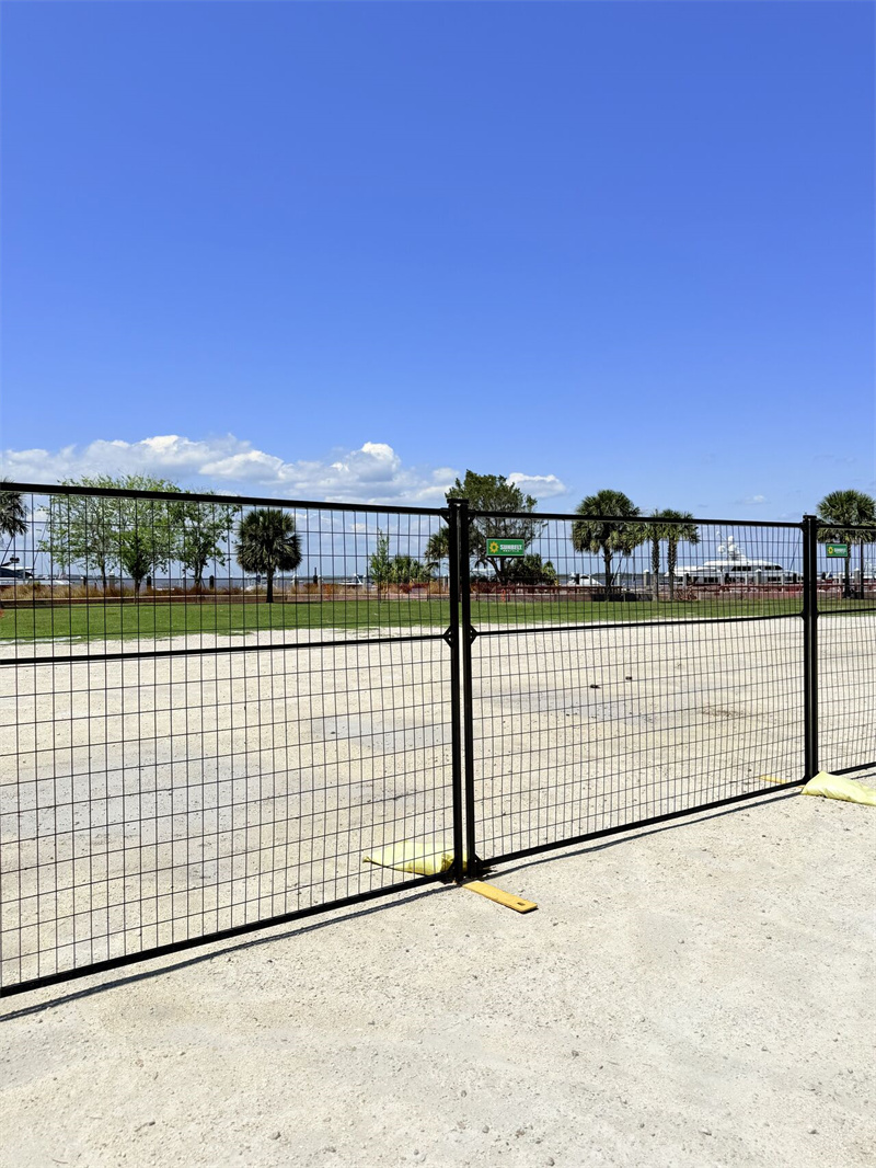 A section of black metal fencing secured to the ground, overlooking a vacant area under a clear blue sky.