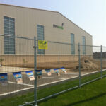 A construction site fence surrounding a building with the sign "Players Paradise" on the wall. The fence has a "VRE Installers Secure Fence Solutions" sign and colorful banners along its length.