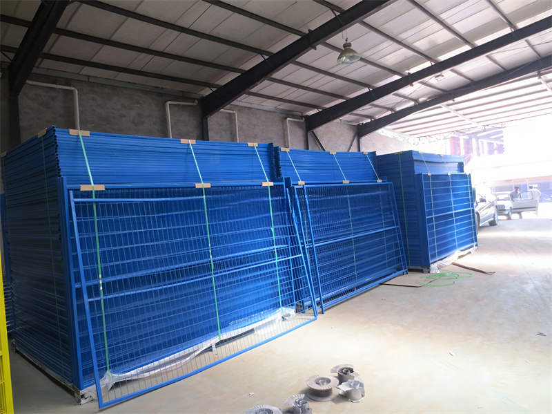 A blue construction fence surrounding a construction site, with equipment and materials visible inside the fenced area, indicating an active work zone.