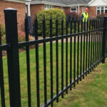 Workers installing a black steel picket fence in front of a suburban home.