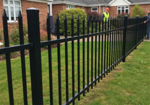 Workers installing a black steel picket fence in front of a suburban home.