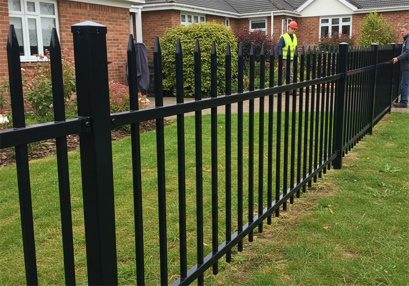Workers installing a black steel picket fence in front of a suburban home.