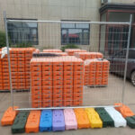 Stacked plastic feet for temporary fencing panels outside a facility, showcasing various colors.