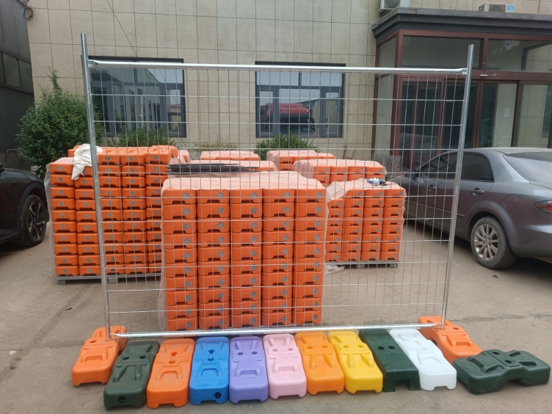Stacked plastic feet for temporary fencing panels outside a facility, showcasing various colors.