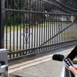 Automated black ornate sliding gate being operated by a car remote control, showcasing convenient access and an external gate motor for residential or commercial use.