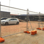 Professional temporary fencing setup with orange concrete stabilizing bases and diagonal braces securing construction site perimeter with parked vehicles