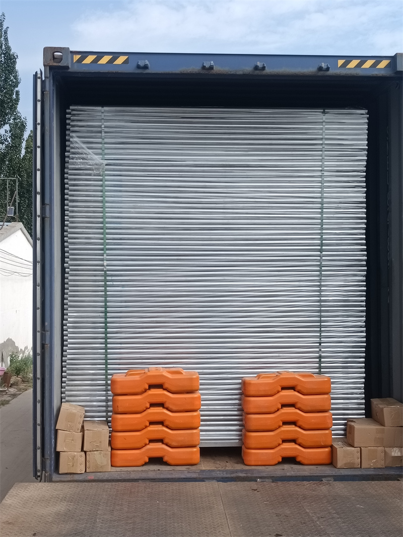 The interior of a shipping container loaded with neatly stacked galvanized temporary fencing panels and two piles of orange plastic fence bases, ready for transportation.