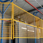 Yellow powder-coated welded wire mesh fence panels hanging on a factory conveyor system.