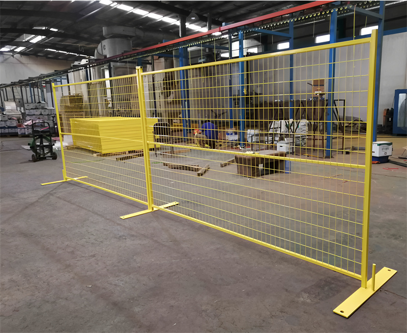 Yellow temporary fence panels with matching flat bases, arranged inside a factory or warehouse, with other yellow components and industrial equipment visible.