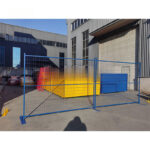 Blue temporary fencing panels installed outside industrial building with metal bases for construction site security