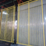 Several yellow mesh temporary fence panels are shown hanging on a production line or rack, likely after a coating process, displaying their grid structure and bright color.
