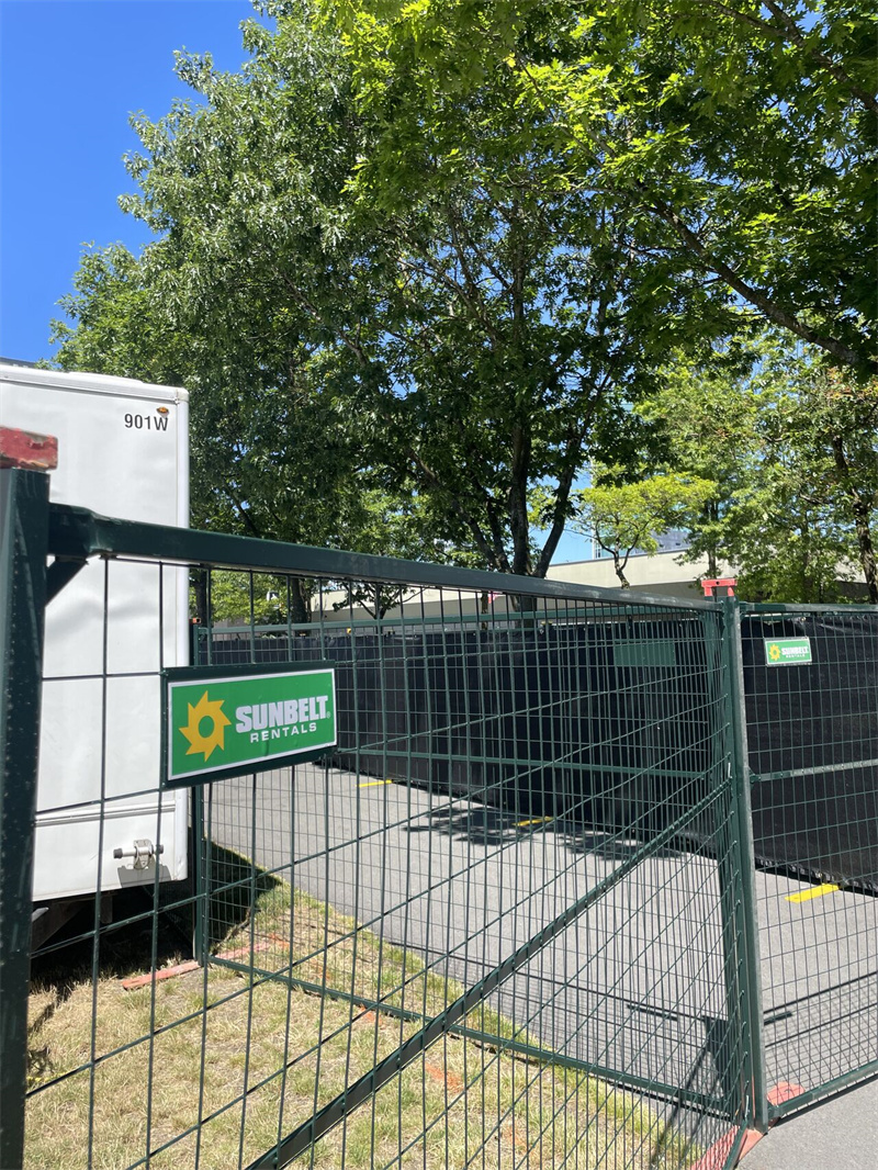 A dark green temporary fence with a gate is shown, featuring a "Sunbelt Rentals" sign. Trees and a white truck are visible in the background.