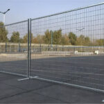 Two galvanized temporary construction fence panels made of welded wire mesh, standing on flat bases on a paved outdoor surface.
